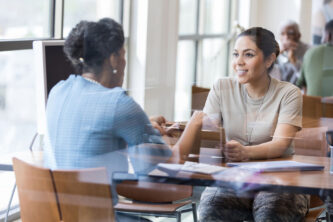 A mature female bank loan officer shows a female veteran a loan application. The veteran attentively listens to the banker