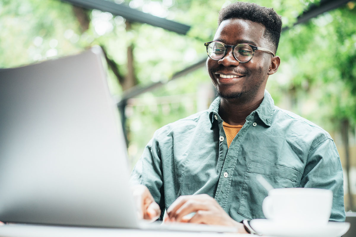 Young afro-american man working outdoor using laptop at sidewalk cafe