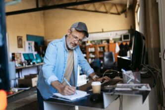 Senior small business owner taking notes and working on computer in workshop