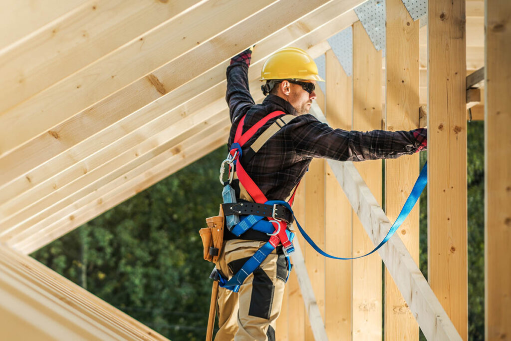 A worker stands on a wooden roof frame at a construction site
